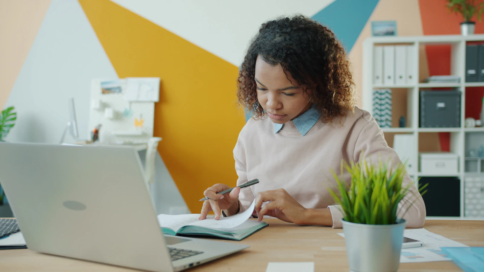 A person at a desk writing notes beside a laptop