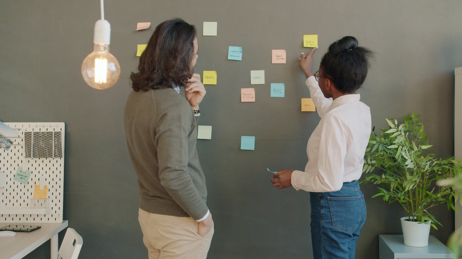Two colleagues talking through a plan in front of a wall of sticky notes